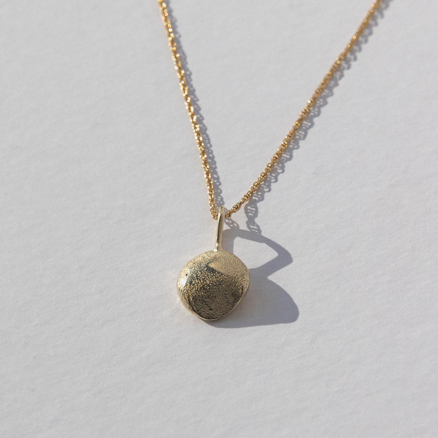 Gold necklace with a round pendant on a light gray background