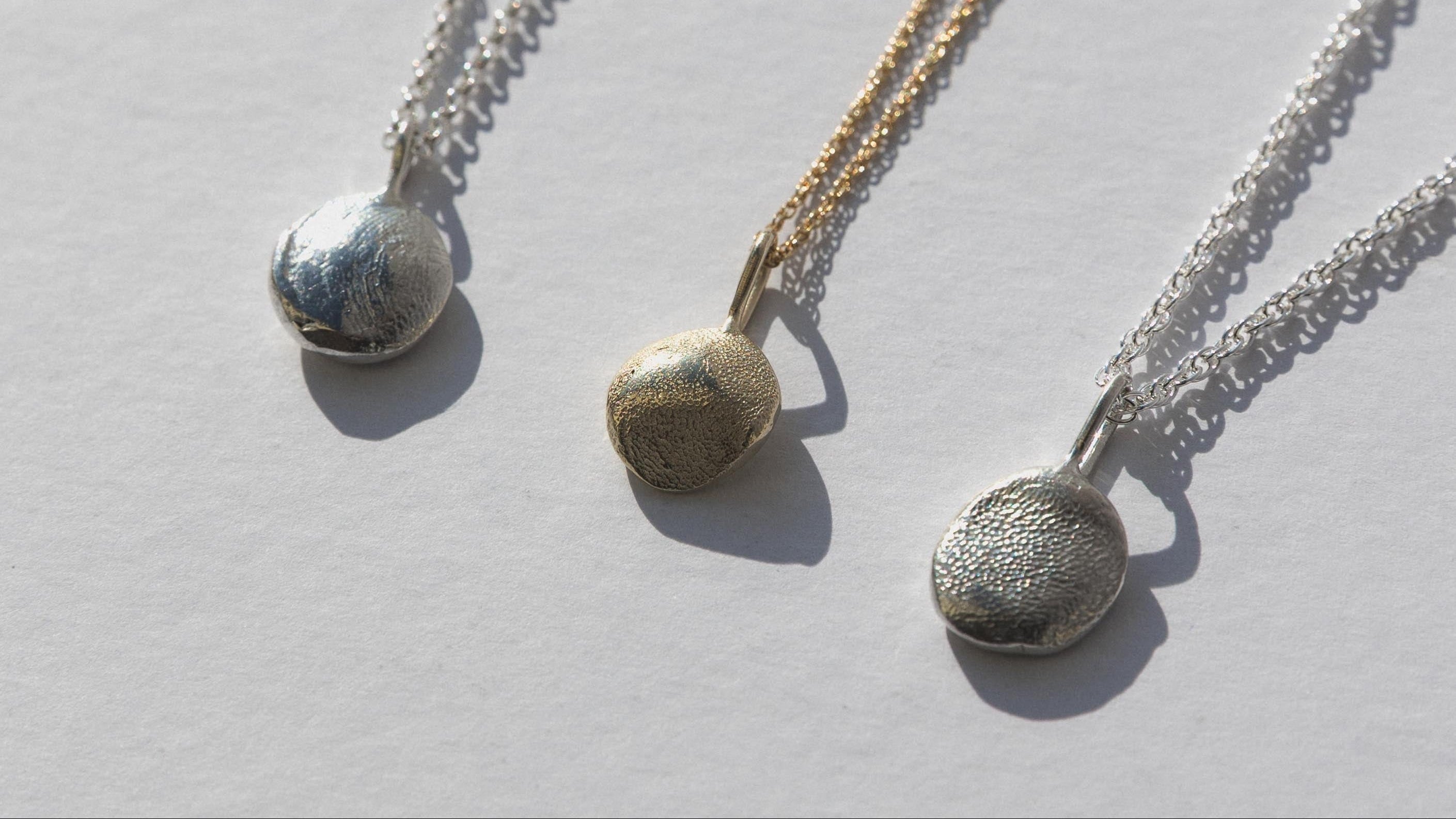 Three silver necklaces with round pendants on a light gray background