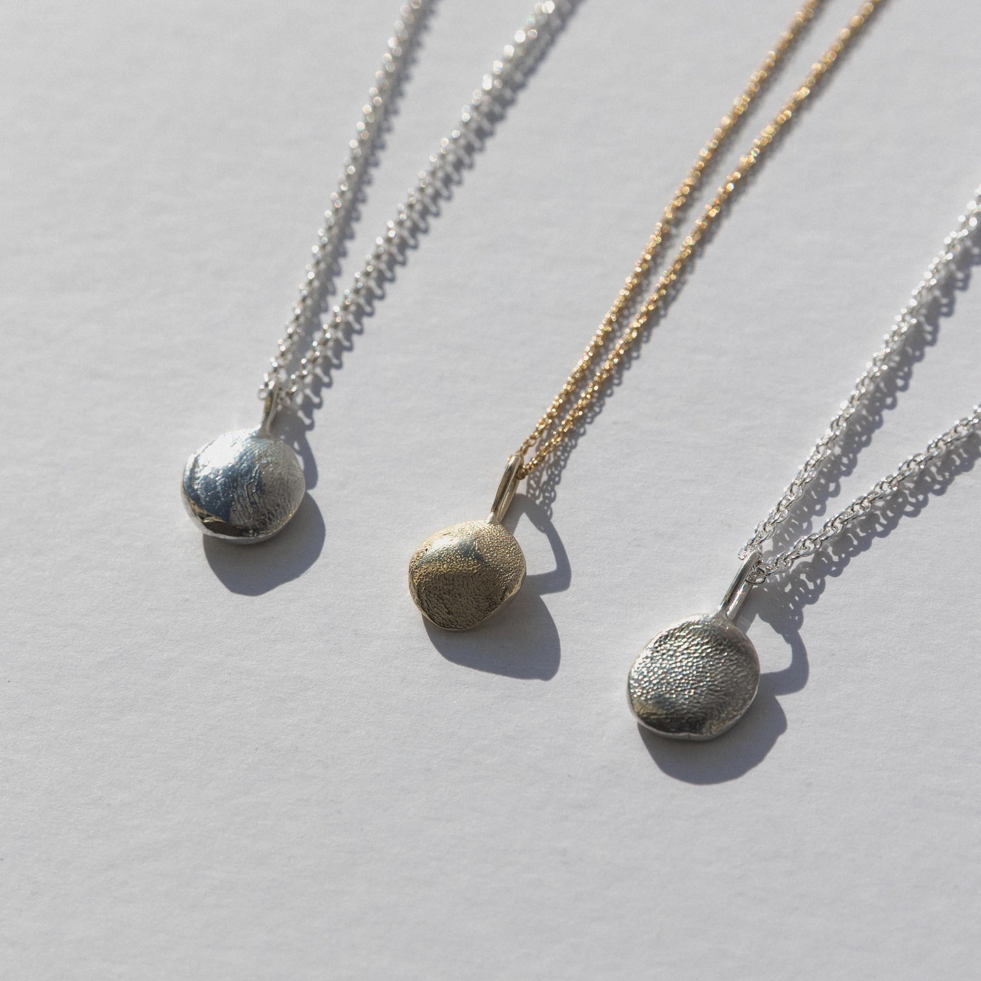 Three silver necklaces with round pendants on a light gray background