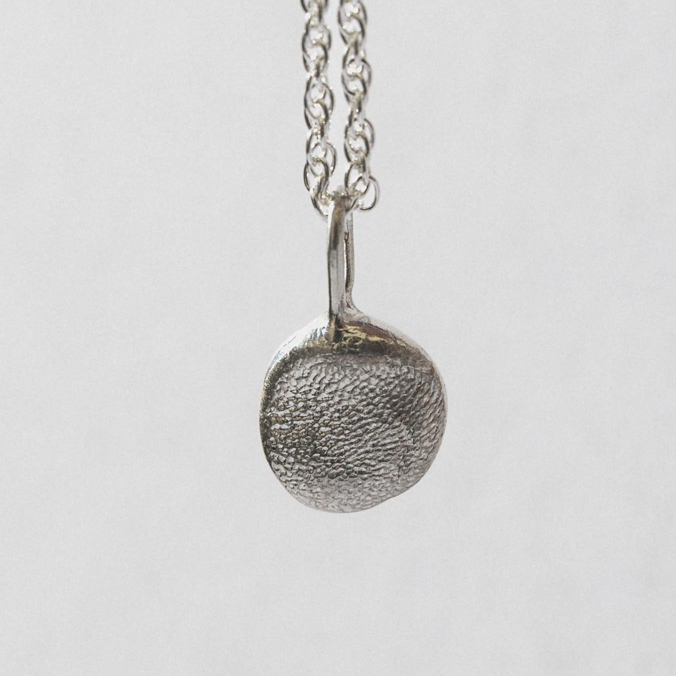 Silver necklace with a textured pendant on a light gray background