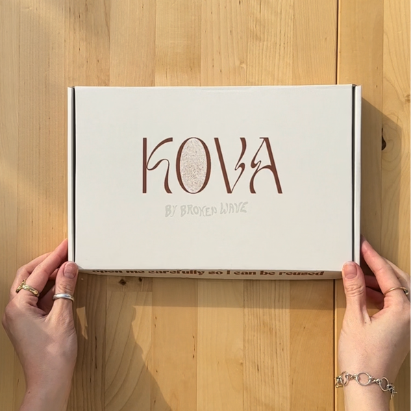 White box with 'Kova' branding held by hands on a wooden surface