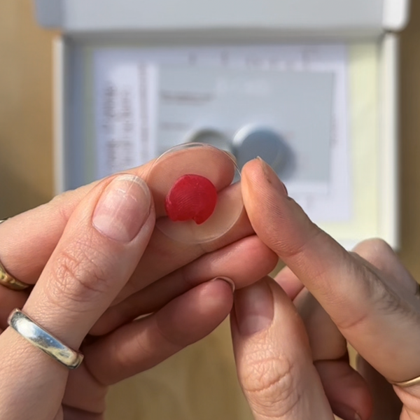 Close-up of a hand holding a small red object with a blurred background